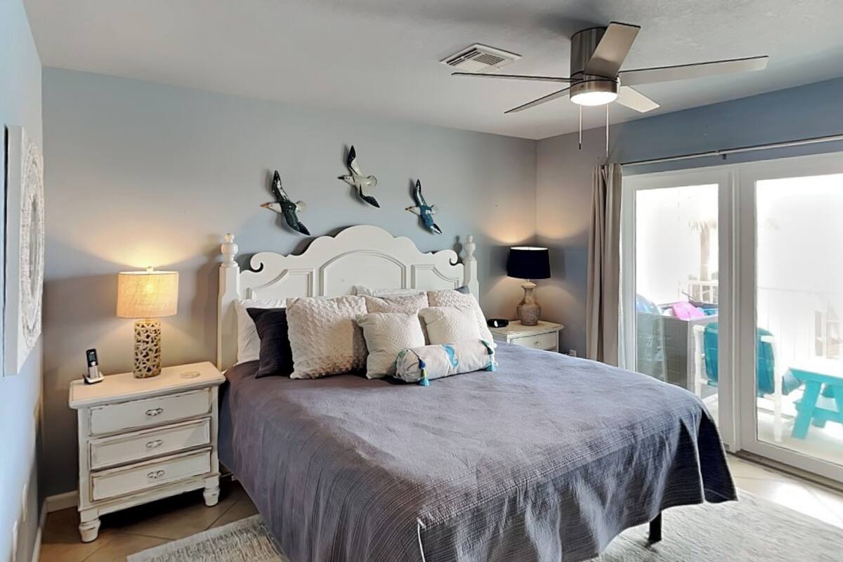 A bedroom with a bed, nightstands, a ceiling fan, and a view through a glass door.
