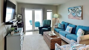 A living room with a television, a sofa, a coffee table, and a painting on the wall. - Grand Caribbean by Silver Sands Vacation Rentals (Port Aransas)