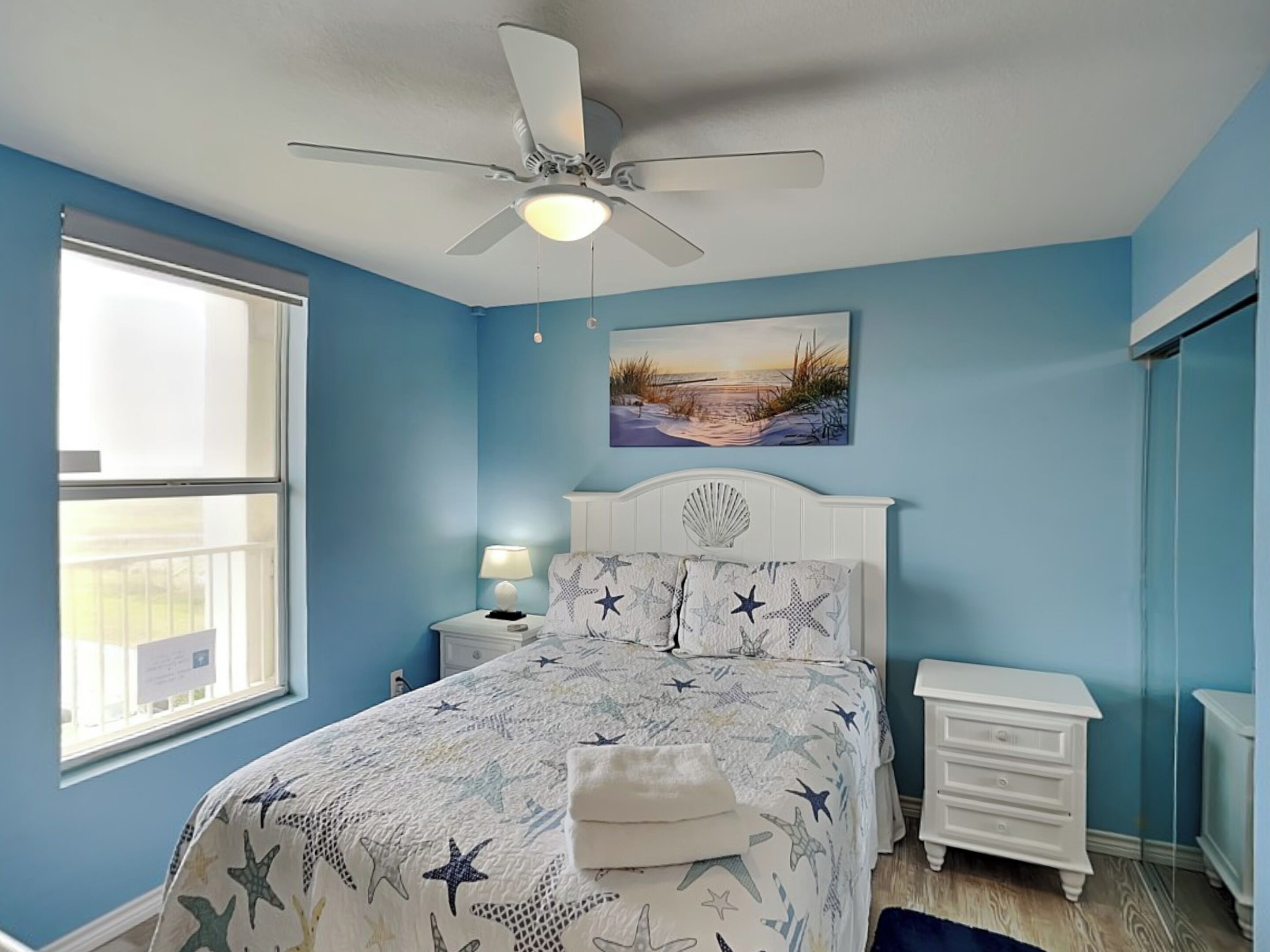 Un dormitorio con cama, mesita de noche, cómoda, ventilador de techo y ventana.