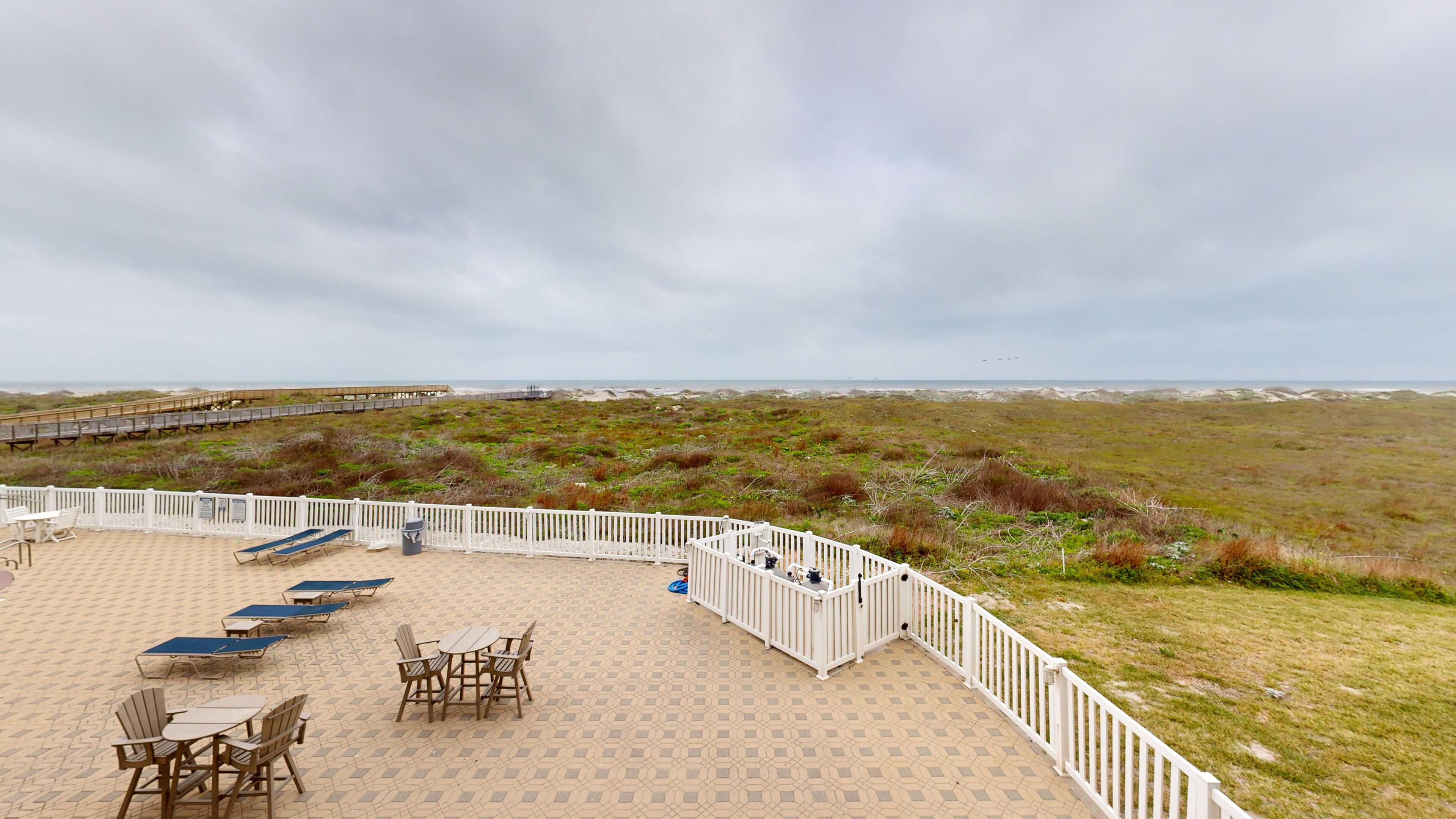 A beachside patio with outdoor seating and a view of the beach and dunes.