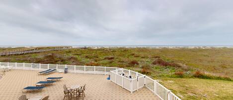 A beachside patio with outdoor seating and a view of the beach and dunes.