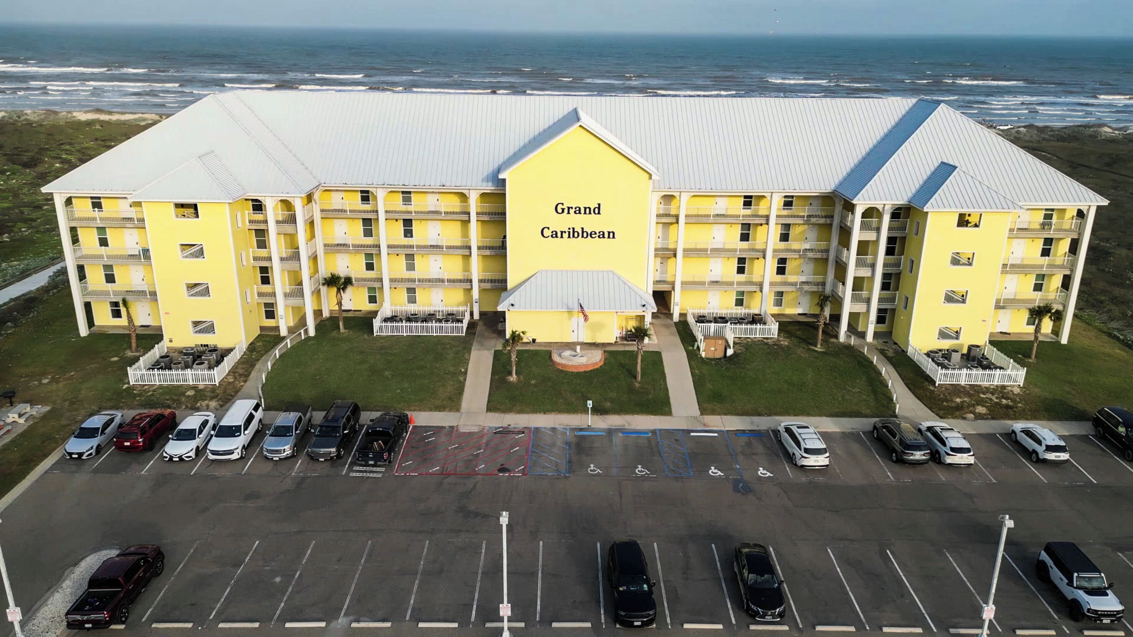 Un hotel grande y amarillo con varios balcones y un estacionamiento frente a él.