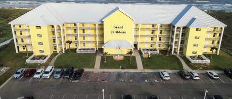 Un hotel grande y amarillo con varios balcones y un estacionamiento frente a él.
