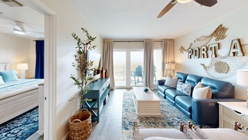 A spacious living area with a blue sofa, a wooden coffee table, and a large window with a view of the outdoors.