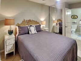 A bedroom with a bed, nightstands, a mirror, and a bathroom visible through an open door.