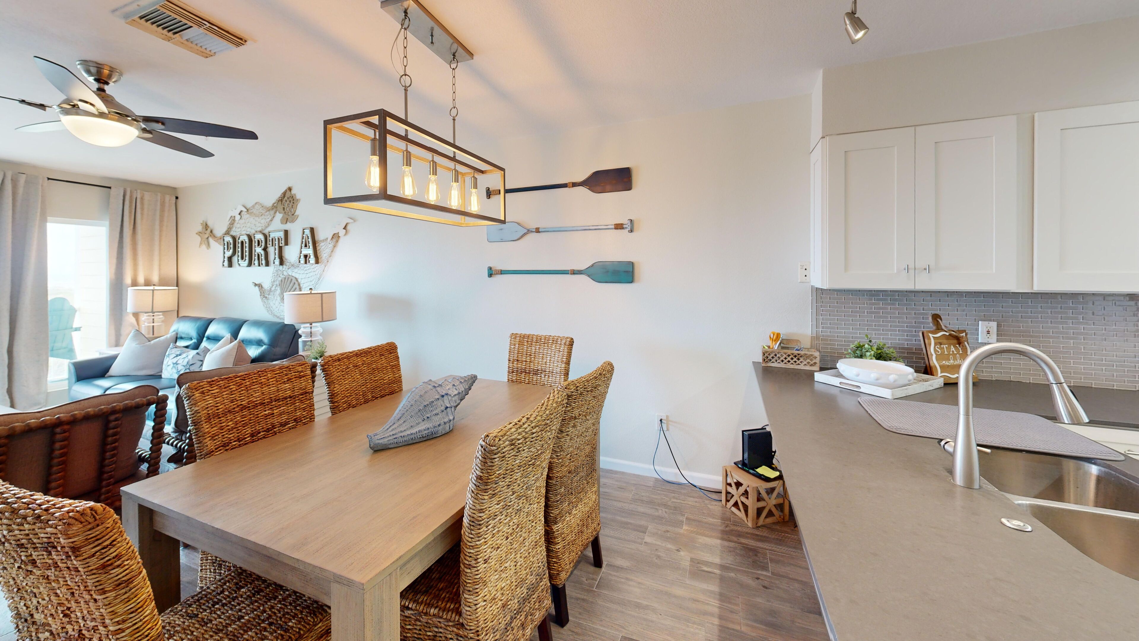 A modern kitchen with a wooden table, wicker chairs, and a hanging light fixture.