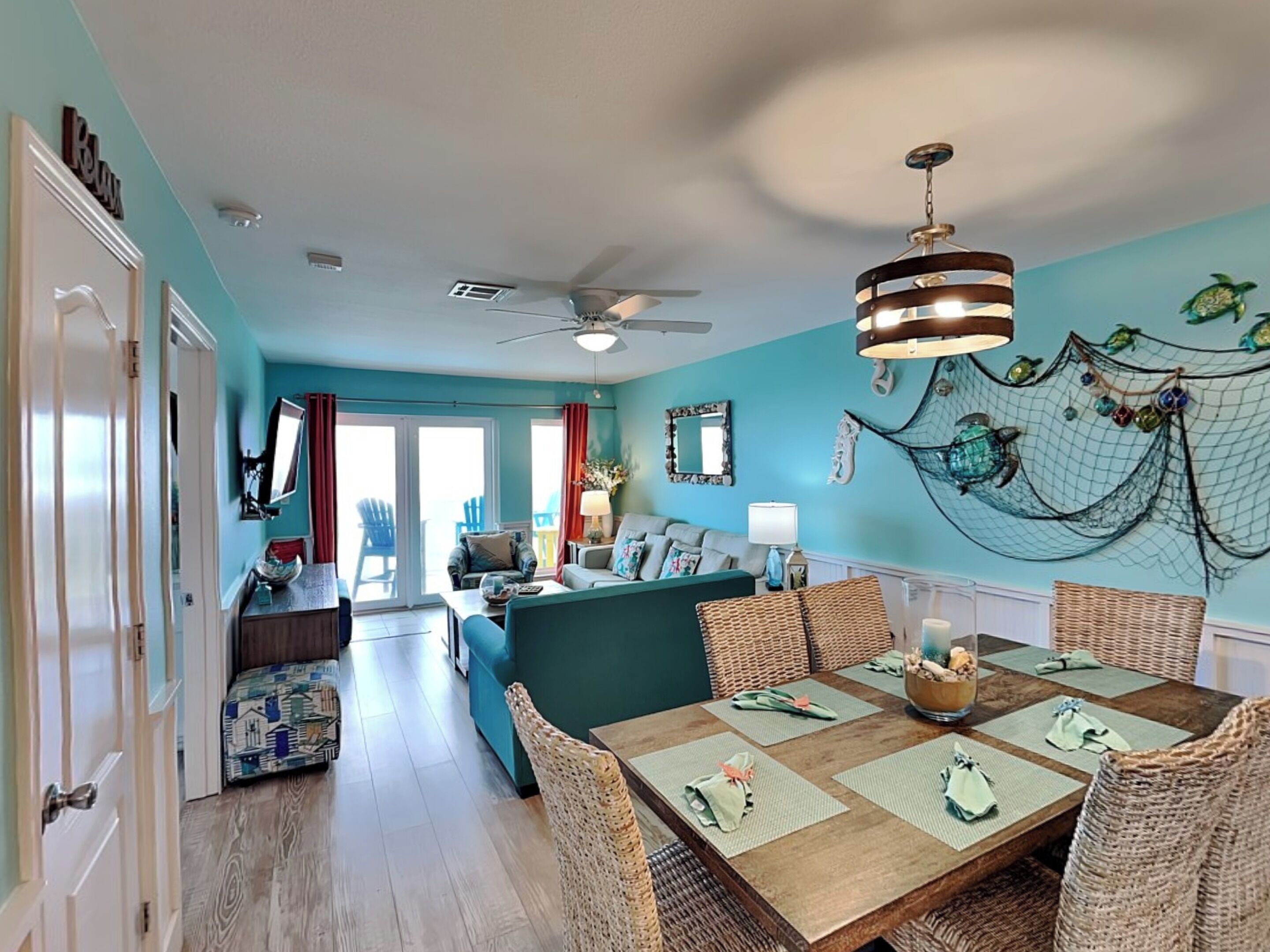 Un'ampia zona giorno con un tavolo da pranzo per quattro persone, una ventola a soffitto e una parete decorata con una rete e pesci.