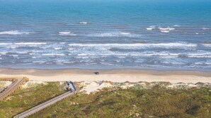 A coastal area with a beach, a bridge, and a car on the sand. - Grand Caribbean by Silver Sands Vacation Rentals (Port Aransas)