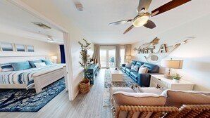 A spacious bedroom with a large bed, a seating area with a sofa and armchairs, a ceiling fan, and a view to the outside. - Grand Caribbean by Silver Sands Vacation Rentals (Port Aransas)