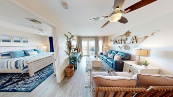 A spacious bedroom with a large bed, a seating area with a sofa and armchairs, a ceiling fan, and a view to the outside.