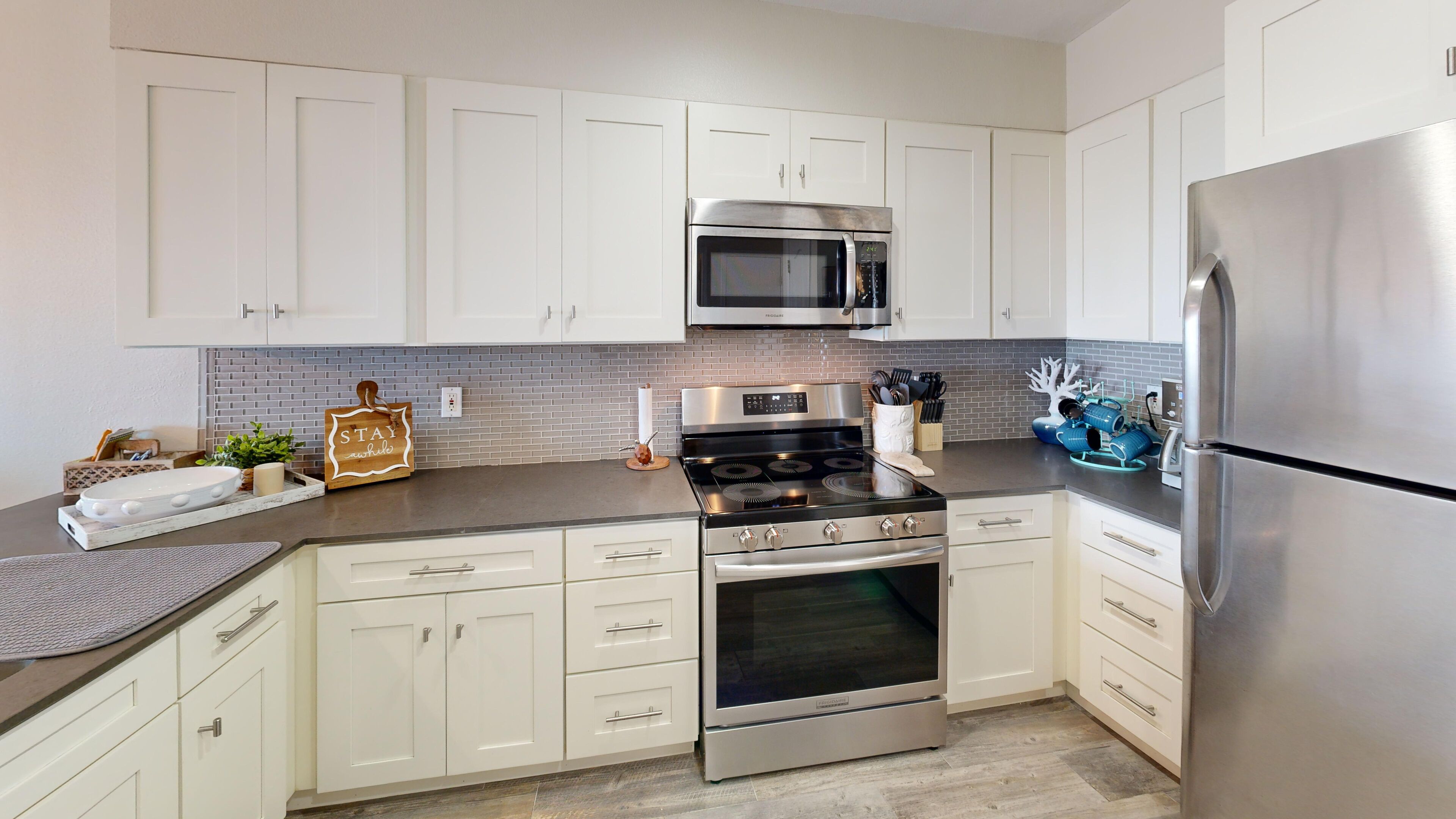 A modern kitchen with white cabinets, stainless steel appliances, and a gray backsplash.