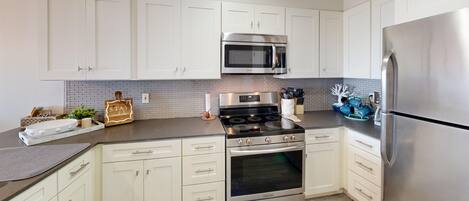 A modern kitchen with white cabinets, stainless steel appliances, and a gray backsplash.