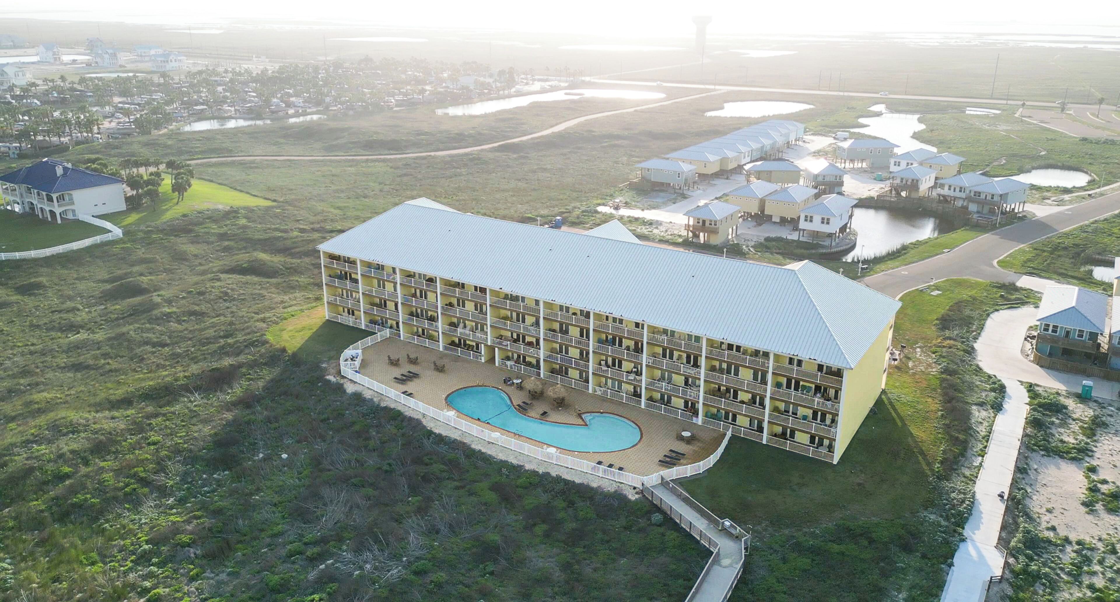 A large hotel with multiple balconies, a swimming pool, and is surrounded by water bodies and greenery.
