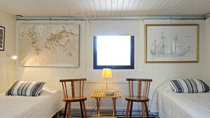 Ein Zimmer mit zwei Einzelbetten, einem kleinen Tisch mit Stühlen, einer Karte und einer an der Wand hängenden Zeichnung eines Schiffes.