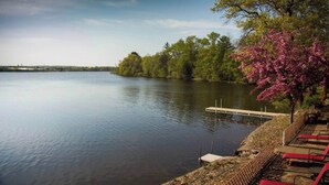 Un lago tranquilo con un muelle que se adentra en el agua, rodeado de árboles y un cielo despejado.