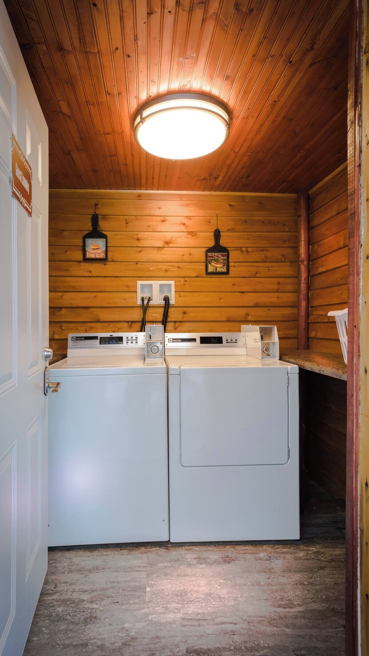 A laundry room with two white washers and dryers, wooden walls, and a ceiling light.