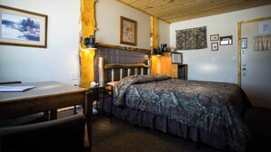 Un dormitorio con cabecera de madera, cama con colcha estampada, escritorio con silla y una lámpara.