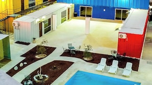 Un hotel con piscina, mobiliario exterior y montañas al fondo.