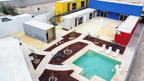 Zona de piscina en la azotea con piscina rectangular, sillas de descanso y un pequeño jardín con plantas y rocas.