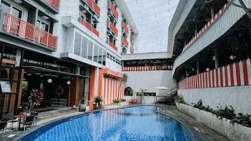 An indoor swimming pool with a view of a multi-story building, a restaurant, and a staircase.