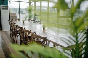 A dining area with a wooden table and chairs, large windows, and indoor plants.