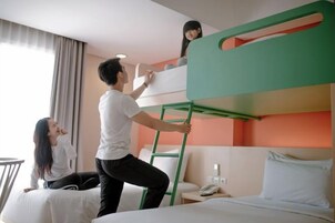 Quarto de hotel com beliches, uma escada, mesa de cabeceira com telefone e janela com cortinas.