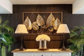 A room with a wooden panel wall, a decorative leaf wall art, a vase with flowers, and two lamps on a white cabinet.