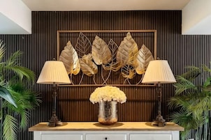 A room with a wooden panel wall, a decorative leaf wall art, a vase with flowers, and two lamps on a white cabinet.