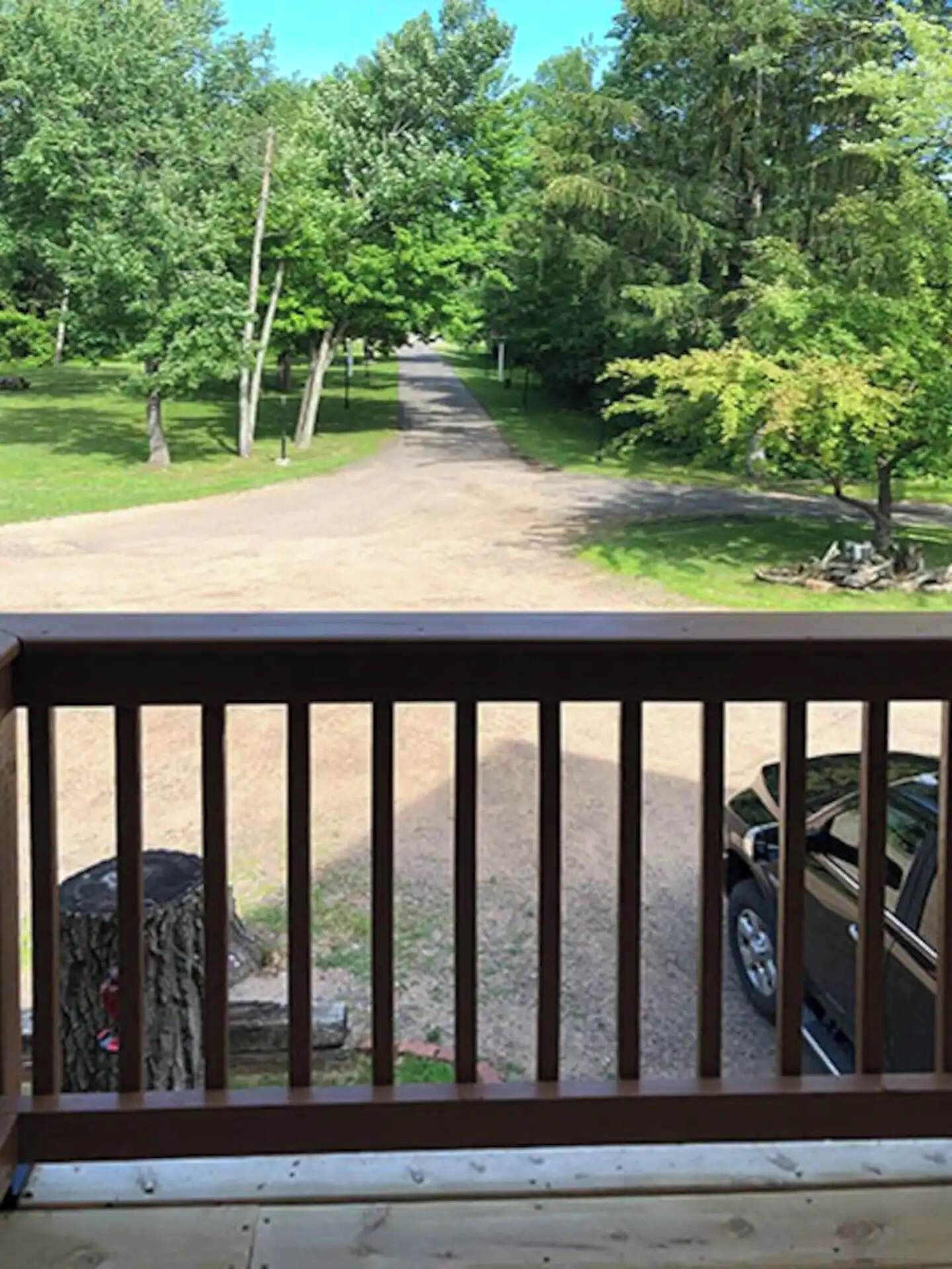 A wooden deck with a view of a dirt path leading through a wooded area.