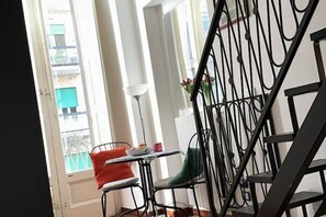 Uma escada com corrimão de metal, uma janela com persianas e uma mesa com cadeiras.