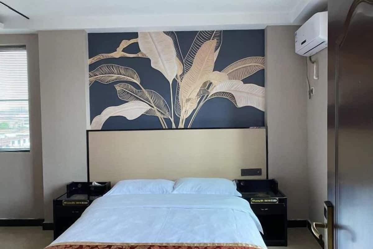 Una habitación de hotel con una cama, una mesita de noche, aire acondicionado de pared y una ventana con persianas.