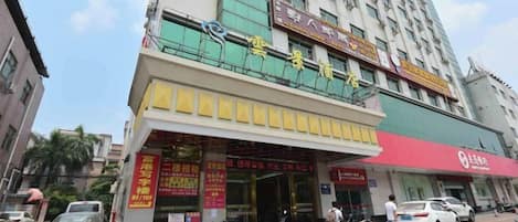 A multi-story building with a ground-level commercial space featuring signage in a foreign language, a red awning, and a parking area with vehicles.