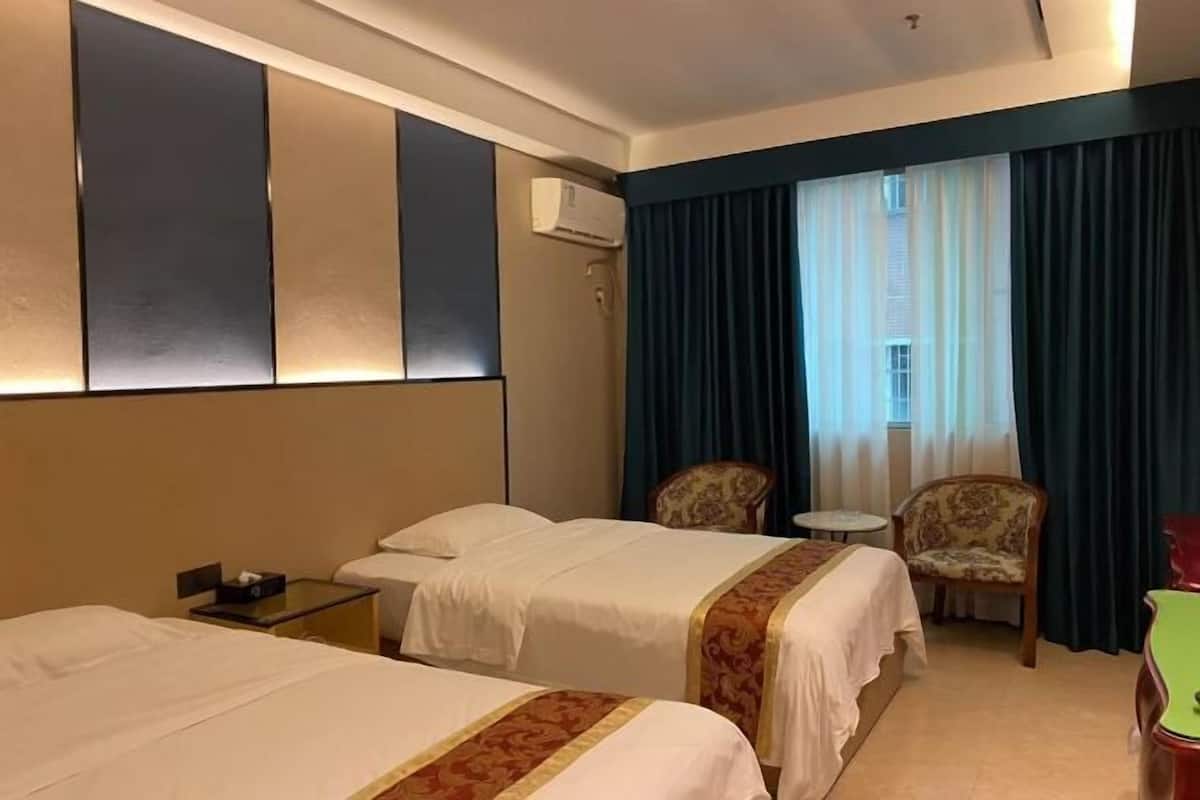 Habitación de hotel con dos camas, una mesita pequeña, dos sillas, una mesita de noche y un ventanal con cortinas.