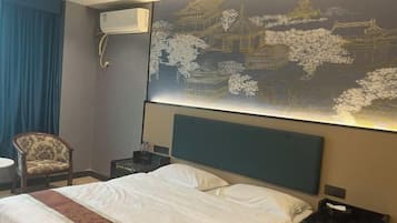 A hotel room with a bed, a chair, a nightstand, and a wall-mounted air conditioner.