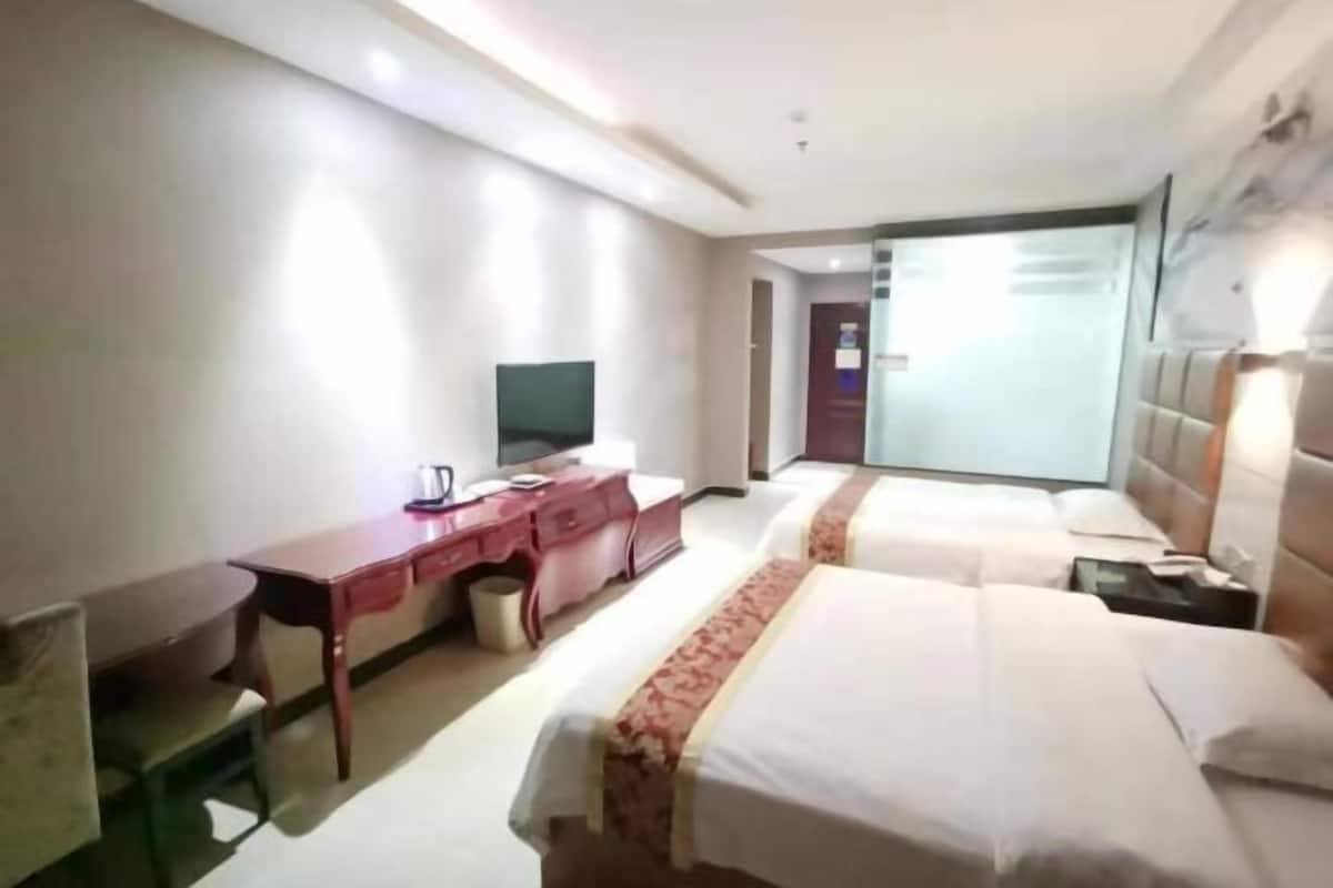 Habitación de hotel con dos camas, un escritorio con silla, televisión y baño a la vista a través de una puerta abierta.