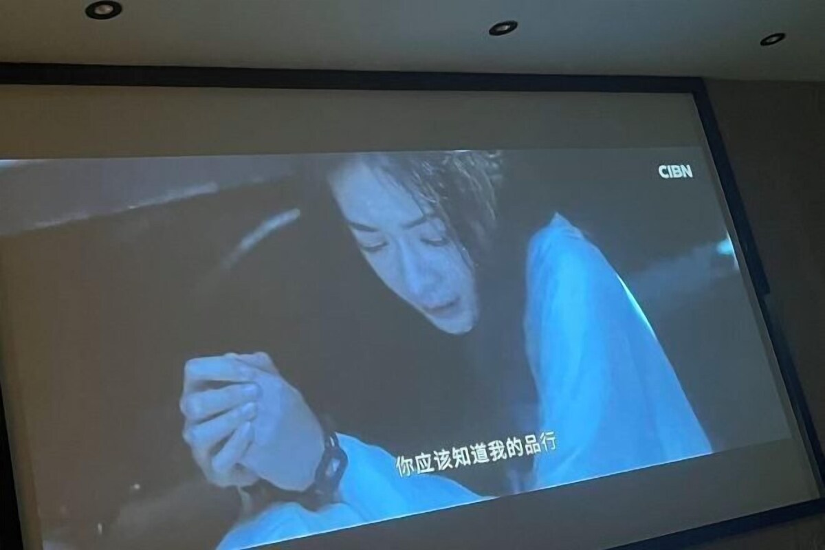 A television screen displaying a scene with a person holding a phone.