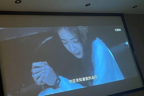 A television screen displaying a scene with a person holding a phone. - Yunjing hotel (Dongguan)