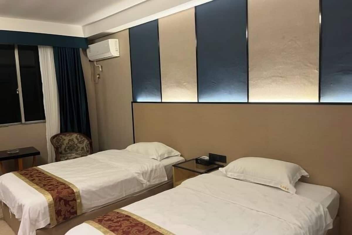 Una habitación de hotel con dos camas individuales, una mesita pequeña, una silla y un aire acondicionado instalado en la pared.