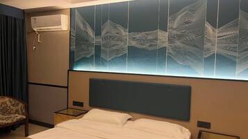Quarto de hotel com uma cama grande, duas mesas de cabeceira, uma cadeira e ar-condicionado fixado na parede.