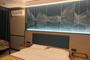 Ett hotellrum med en stor säng, två sängbord, en stol och en väggmonterad luftkonditioneringsanläggning.