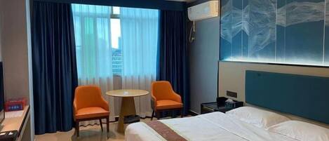 A hotel room with a bed, two chairs, a small table, and a large window with curtains.