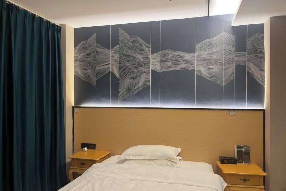 Habitación de hotel con cama, dos mesitas de noche, una obra de arte abstracta grande en la pared y una cortina azul.