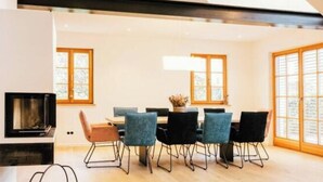 A modern living room with a high ceiling, a fireplace, a dining area with chairs, and large windows. - Cloud 9A Comfortable Holiday Residence (Traunstein)