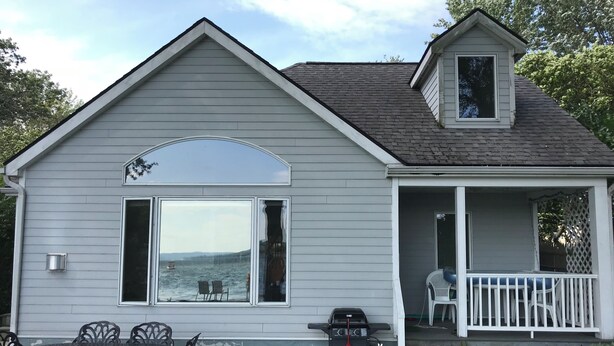 A small, single-story house with a covered porch and a view of the water. - North Shore, Conesus Lake (Lakeville)