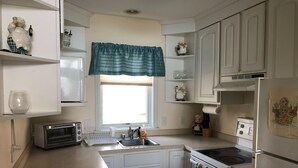 A kitchen with white cabinets, a window with a blue valance, a toaster, a sink, and a stove. - North Shore, Conesus Lake (Lakeville)