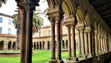 Una serie de columnas de piedra con intrincados grabados, que conducen a un patio con una palmera y un edificio al fondo.