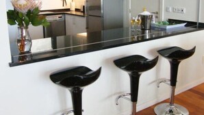 A modern kitchen with a large mirror, stainless steel appliances, and three black bar stools.