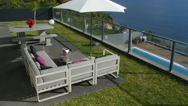 A balcony with a white sofa, a table with a potted plant, and a view of the ocean.