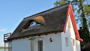 A white building with a thatched roof and a red chimney, featuring a circular window and a small porch. - Holiday House House by the Lake (Krakow am See)