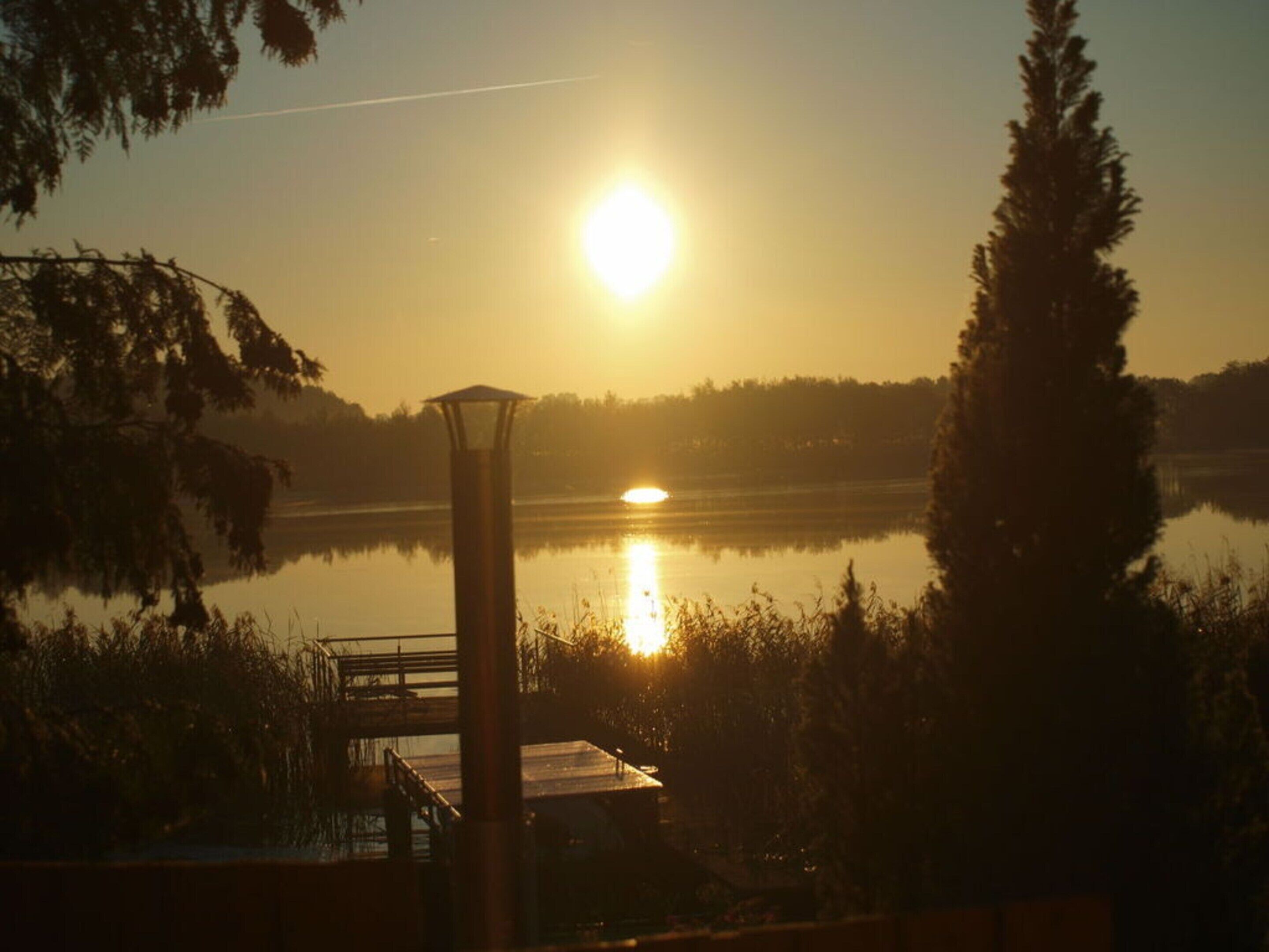 A sunrise over a calm lake with a dock and a gazebo.